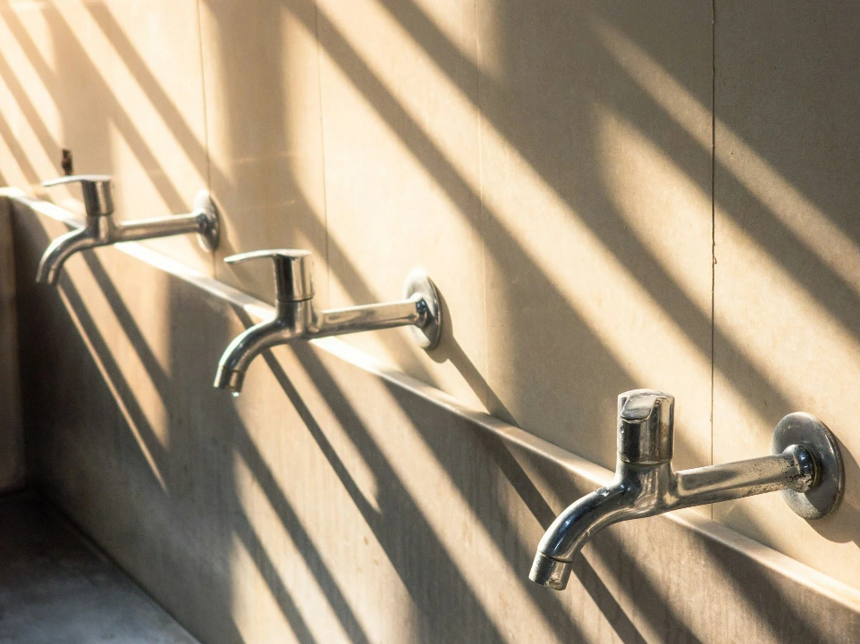 Three faucets aligned against a wall with shadows.